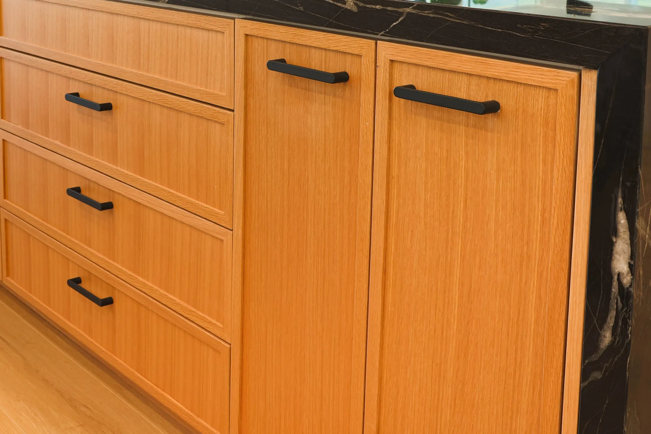 Close-up of kitchen cabinet drawers with dark handles and vertical wood grain